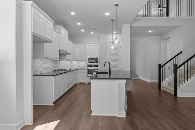 kitchen with tasteful backsplash, dark countertops, appliances with stainless steel finishes, dark wood finished floors, and under cabinet range hood