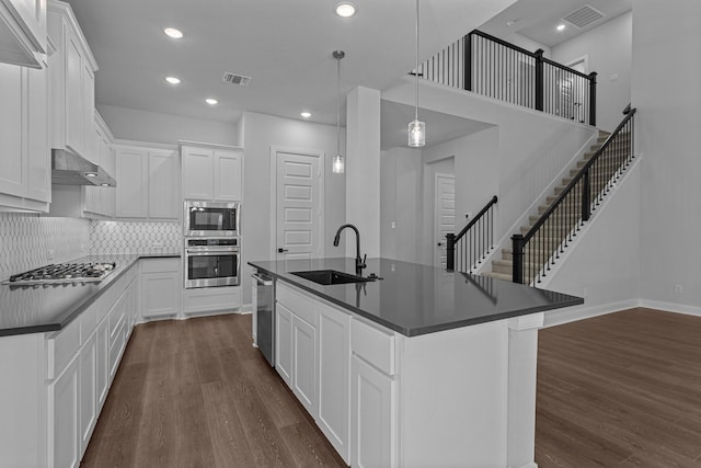 kitchen with dark countertops, visible vents, wall chimney exhaust hood, appliances with stainless steel finishes, and a sink