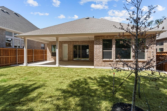 rear view of property with a lawn, a patio area, brick siding, fence, and a shingled roof