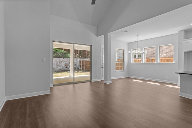 unfurnished living room with dark wood-style flooring, baseboards, vaulted ceiling, visible vents, and ceiling fan with notable chandelier