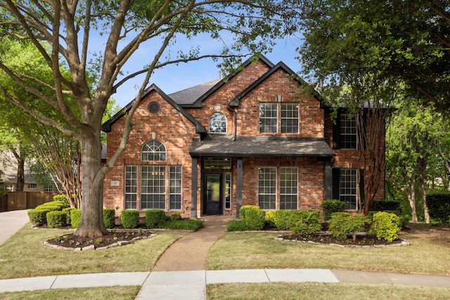 traditional-style home featuring fence, a shingled roof, a front lawn, and brick siding