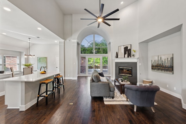living room with dark wood-style floors, baseboards, a fireplace, high vaulted ceiling, and ceiling fan with notable chandelier
