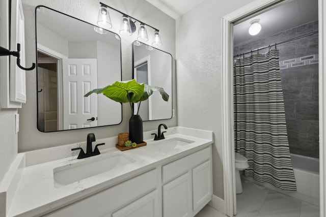 full bath featuring marble finish floor, double vanity, a textured wall, toilet, and a sink