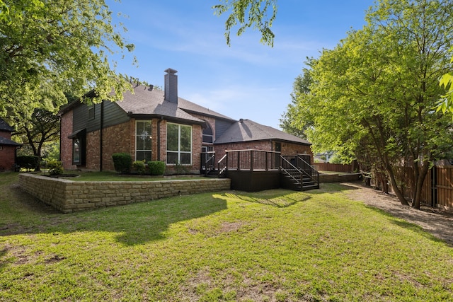 back of house featuring a chimney, fence, brick siding, a lawn, and a deck