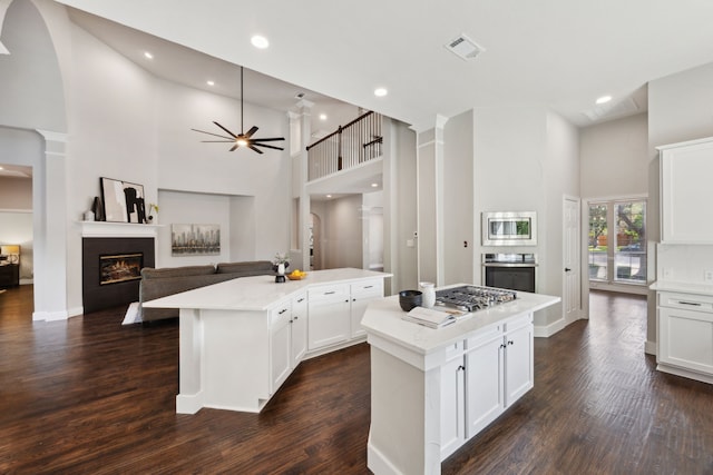 kitchen featuring a towering ceiling, visible vents, a center island, a glass covered fireplace, and appliances with stainless steel finishes
