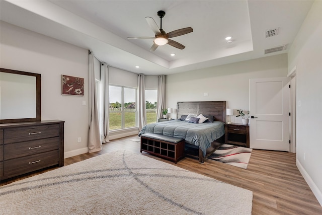 bedroom featuring visible vents, baseboards, a raised ceiling, and wood finished floors