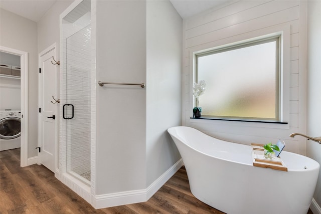 bathroom featuring a shower stall, washer / dryer, a soaking tub, and wood finished floors