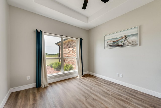 unfurnished room featuring baseboards, a ceiling fan, a raised ceiling, and wood finished floors