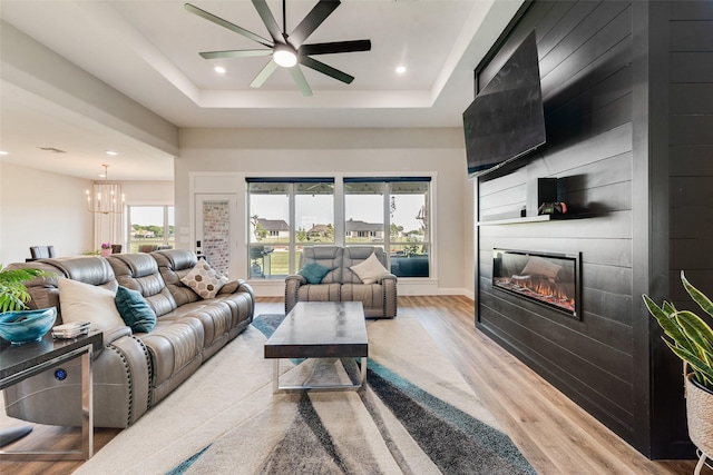 living area featuring ceiling fan with notable chandelier, a fireplace, recessed lighting, wood finished floors, and a raised ceiling