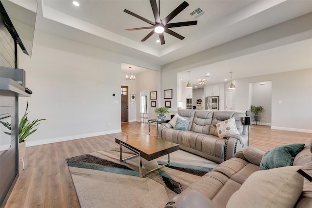 living area with light wood-style flooring, ceiling fan with notable chandelier, a tray ceiling, and recessed lighting