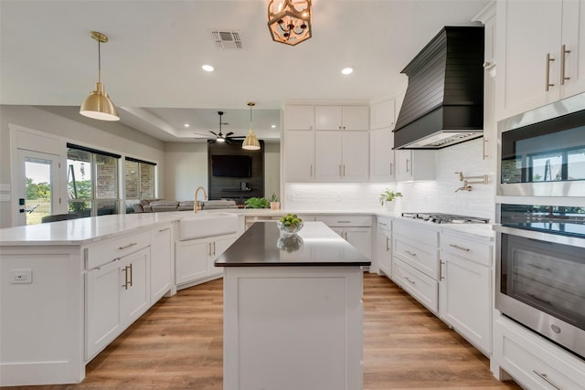 kitchen featuring custom exhaust hood, visible vents, a sink, appliances with stainless steel finishes, and a kitchen island