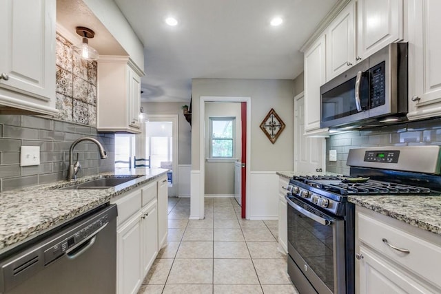 kitchen with a sink, white cabinetry, appliances with stainless steel finishes, decorative backsplash, and light tile patterned flooring