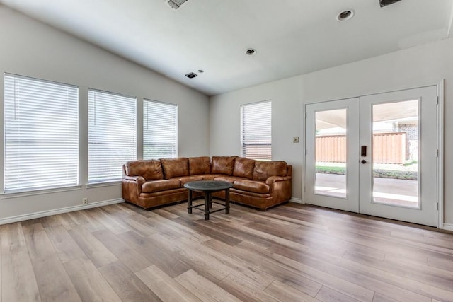 living room featuring vaulted ceiling, light wood-type flooring, baseboards, and french doors