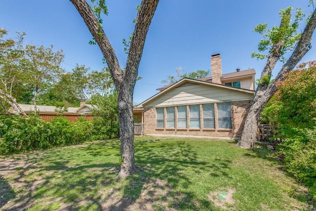 back of property featuring brick siding, fence, and a lawn
