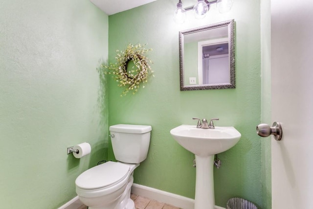 half bath with toilet, tile patterned flooring, baseboards, and a sink
