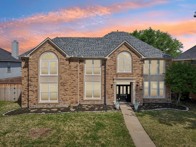 view of front facade with a front lawn, a shingled roof, french doors, and brick siding