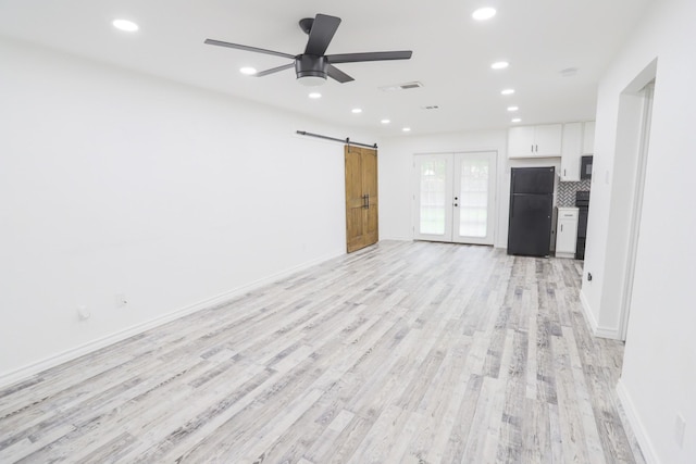 unfurnished living room with recessed lighting, a barn door, light wood-style floors, and french doors