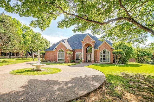 view of front of house featuring a front lawn, brick siding, and a shingled roof