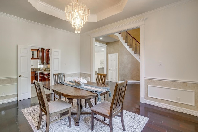 dining room featuring a wainscoted wall, a tray ceiling, dark wood finished floors, a notable chandelier, and ornamental molding