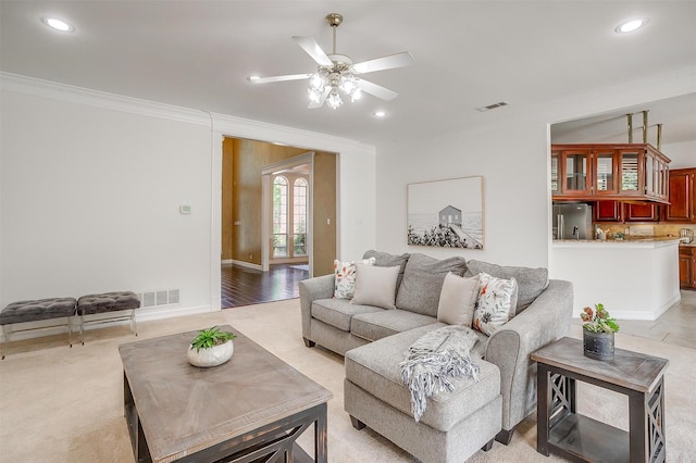 living area with ceiling fan, ornamental molding, and visible vents