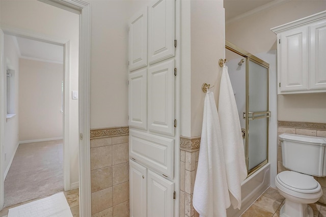 full bath with tile walls, a wainscoted wall, shower / bath combination with glass door, and toilet