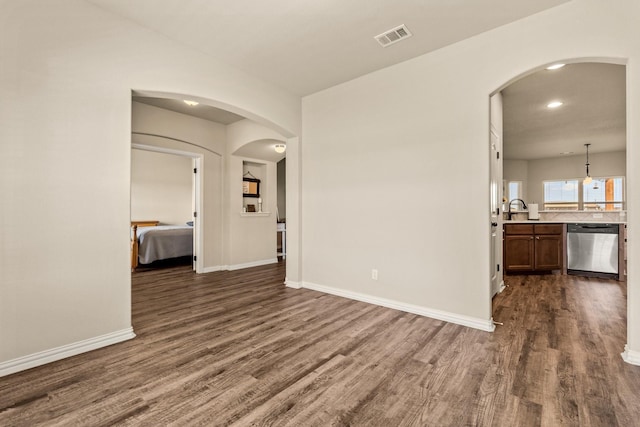 empty room with arched walkways, dark wood-style flooring, baseboards, and visible vents