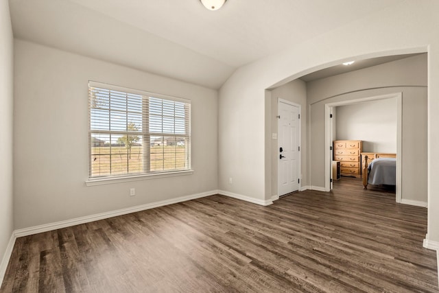 spare room with arched walkways, lofted ceiling, baseboards, and dark wood finished floors