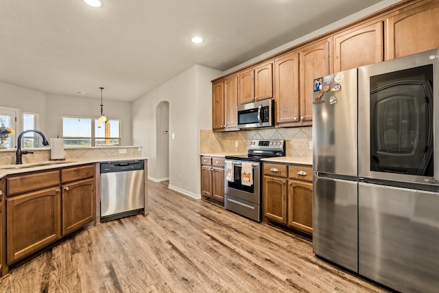 kitchen with arched walkways, a sink, light countertops, appliances with stainless steel finishes, and light wood-style floors
