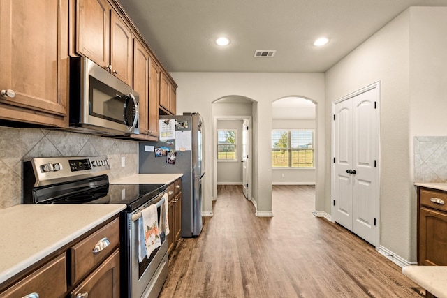 kitchen with tasteful backsplash, visible vents, appliances with stainless steel finishes, arched walkways, and wood finished floors