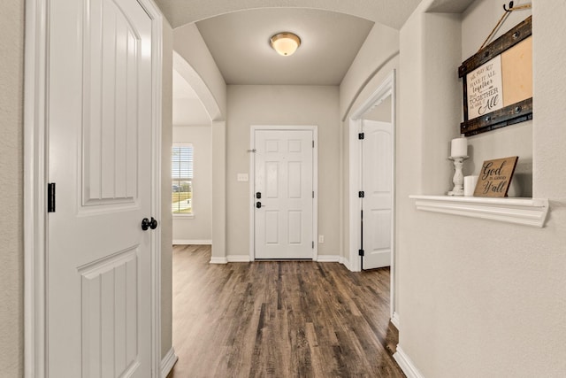 interior space with arched walkways, dark wood-type flooring, and baseboards