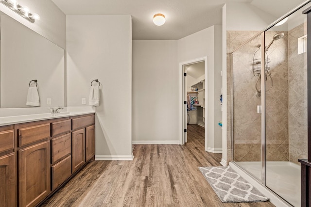 full bathroom with a spacious closet, a stall shower, wood finished floors, and vanity