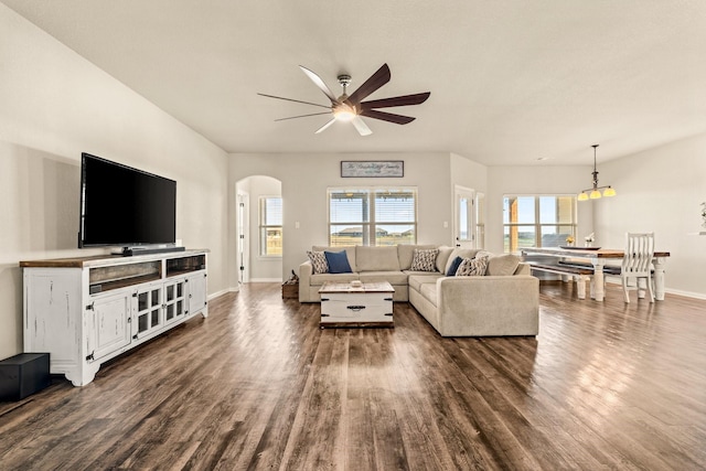 living room featuring arched walkways, dark wood-style flooring, a ceiling fan, and a wealth of natural light