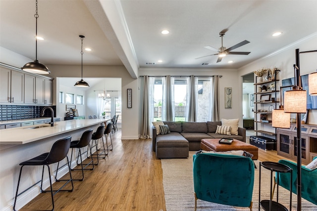 living area with light wood-style floors, ceiling fan with notable chandelier, crown molding, and a healthy amount of sunlight