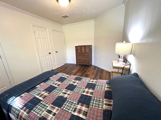 bedroom with a closet, ornamental molding, a textured ceiling, visible vents, and wood finished floors