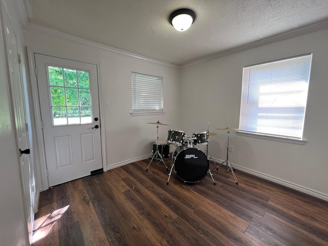 recreation room with baseboards, a textured ceiling, ornamental molding, and dark wood finished floors
