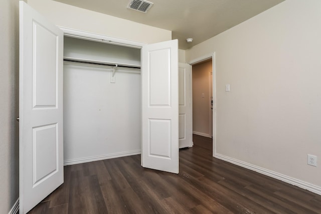 unfurnished bedroom featuring dark wood-style flooring, visible vents, baseboards, and a closet