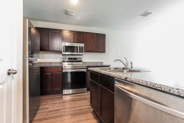 kitchen featuring light wood-style floors, dark brown cabinetry, visible vents, appliances with stainless steel finishes, and a sink