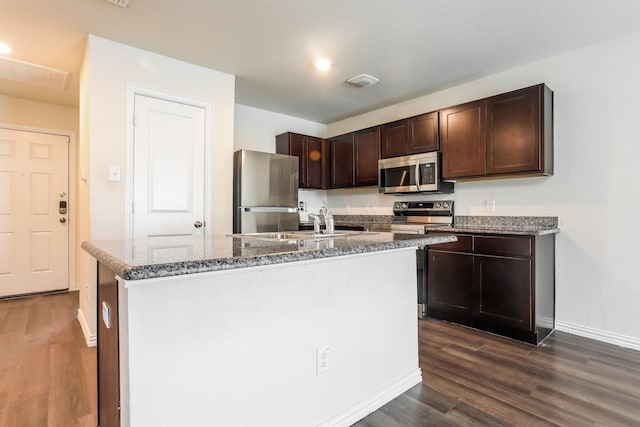 kitchen with dark brown cabinetry, baseboards, dark wood-style floors, a center island with sink, and stainless steel appliances