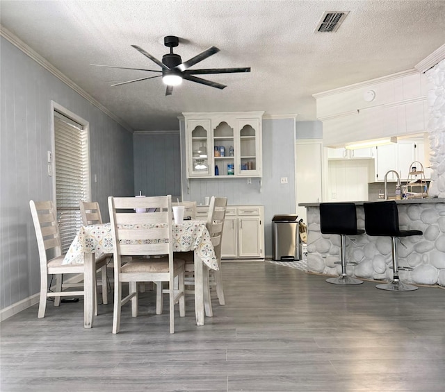 dining area with dark wood-style flooring, crown molding, a ceiling fan, visible vents, and a textured ceiling