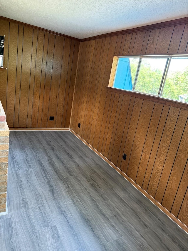 unfurnished room with wood walls, a textured ceiling, wood finished floors, and baseboards