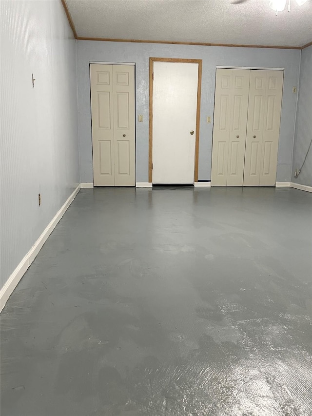 unfurnished bedroom with a textured ceiling, finished concrete floors, ornamental molding, and baseboards
