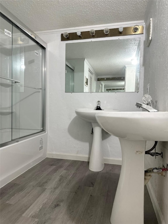full bath featuring a textured ceiling, shower / bath combination with glass door, a textured wall, baseboards, and wood finished floors