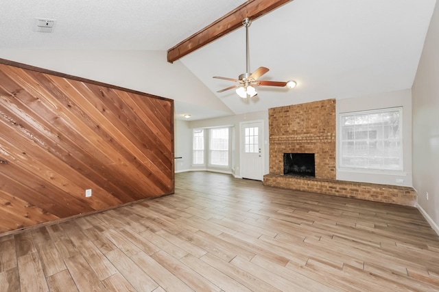 unfurnished living room featuring baseboards, lofted ceiling with beams, a ceiling fan, a brick fireplace, and light wood finished floors
