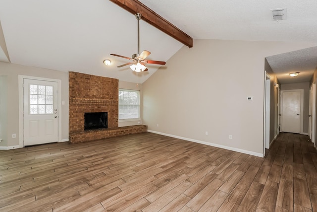 unfurnished living room with lofted ceiling with beams, a ceiling fan, a brick fireplace, visible vents, and wood finished floors