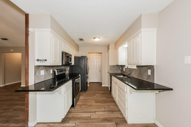 kitchen with white cabinets, a sink, dark countertops, light wood-type flooring, and appliances with stainless steel finishes
