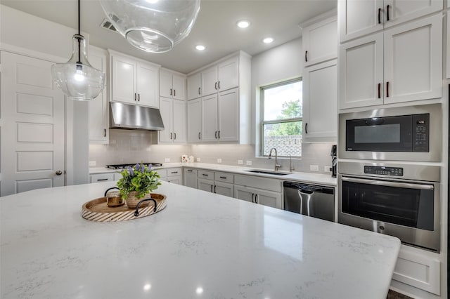 3128 Lexington Dr, Celina, TX 75009 - kitchen featuring appliances with stainless steel finishes, under cabinet range hood, white cabinets, tasteful backsplash, and decorative light fixtures