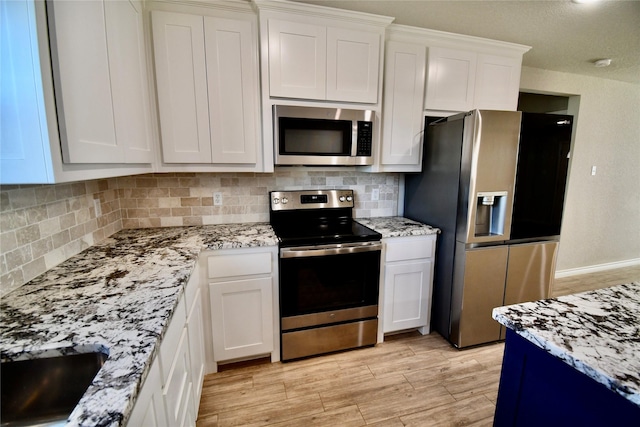 kitchen with tasteful backsplash, white cabinets, appliances with stainless steel finishes, light wood finished floors, and light stone countertops