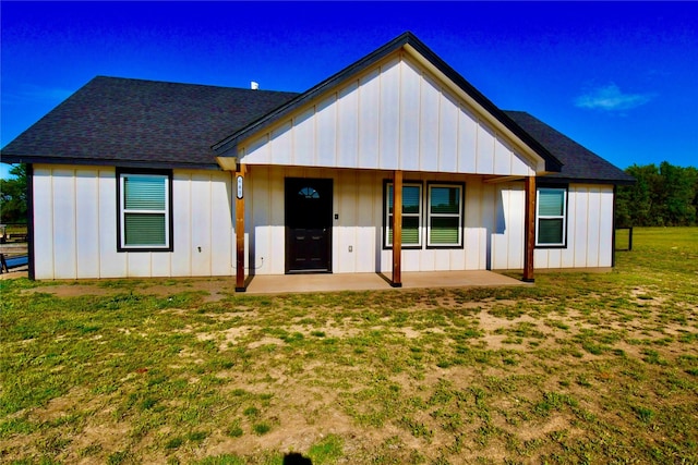 back of property with board and batten siding, a shingled roof, a patio, and a yard