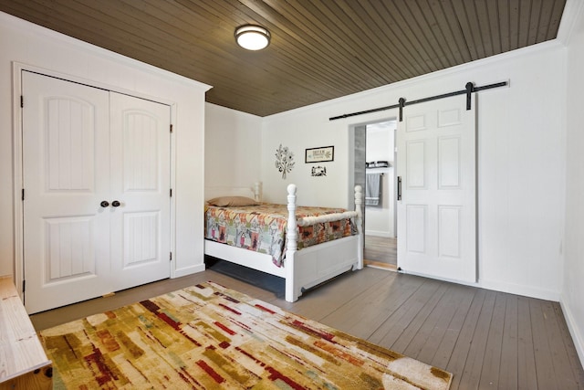 bedroom with crown molding, a closet, a barn door, baseboards, and hardwood / wood-style flooring