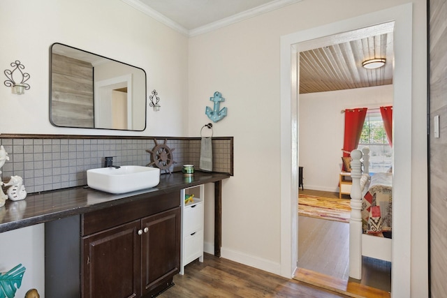 bathroom with baseboards, ornamental molding, vanity, wood finished floors, and decorative backsplash